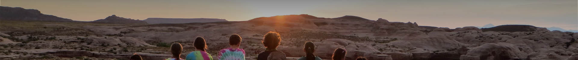 Group sitting on rock formation staring into the distance, away from camera, during sunset